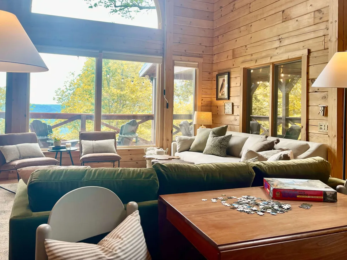 A cozy seating area with expansive windows opening to serene outdoor views, a rustic wooden interior, and a puzzle in progress on the table. The inviting space is set for shared activities and intimate moments, emphasizing relaxation, interaction, and a harmonious connection with nature.