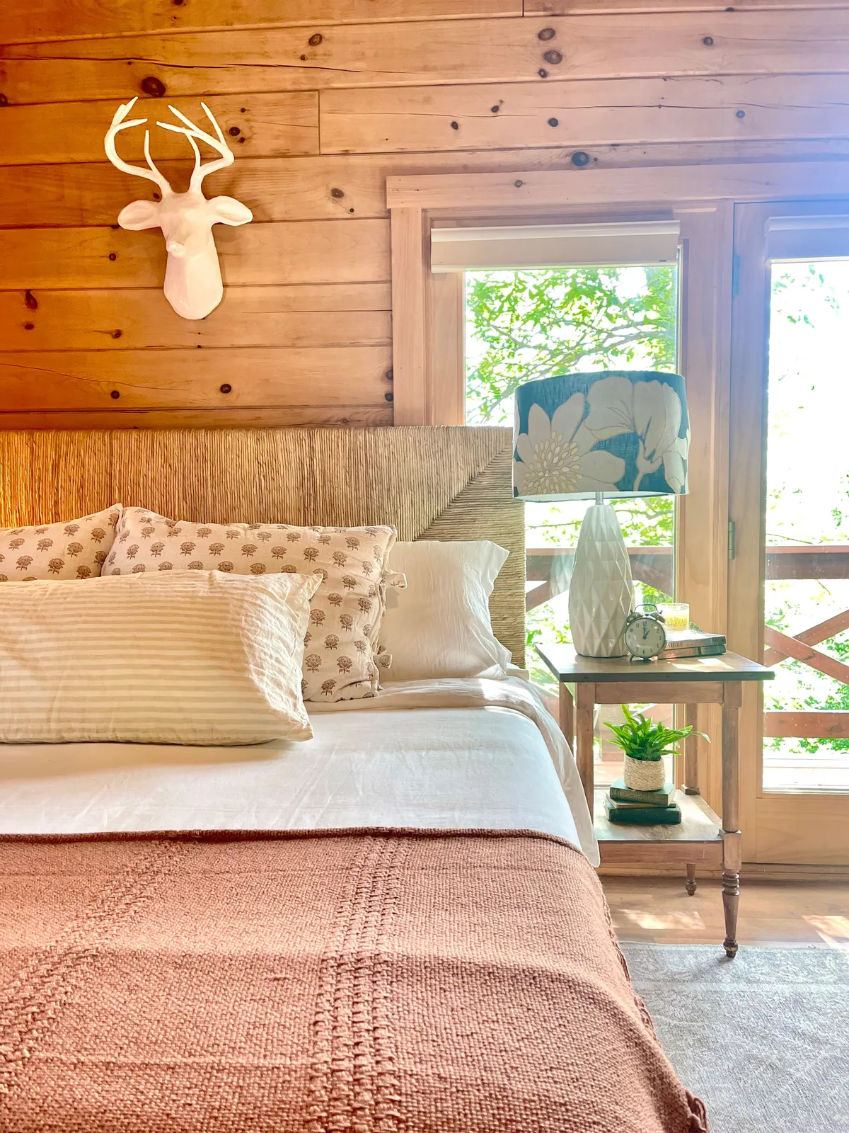 A warm, inviting bedroom with a bed topped with pillows and a throw blanket, a decorative lamp on the nightstand, and a window letting in soft natural light. The decor conveys an atmosphere of peace and relaxation.