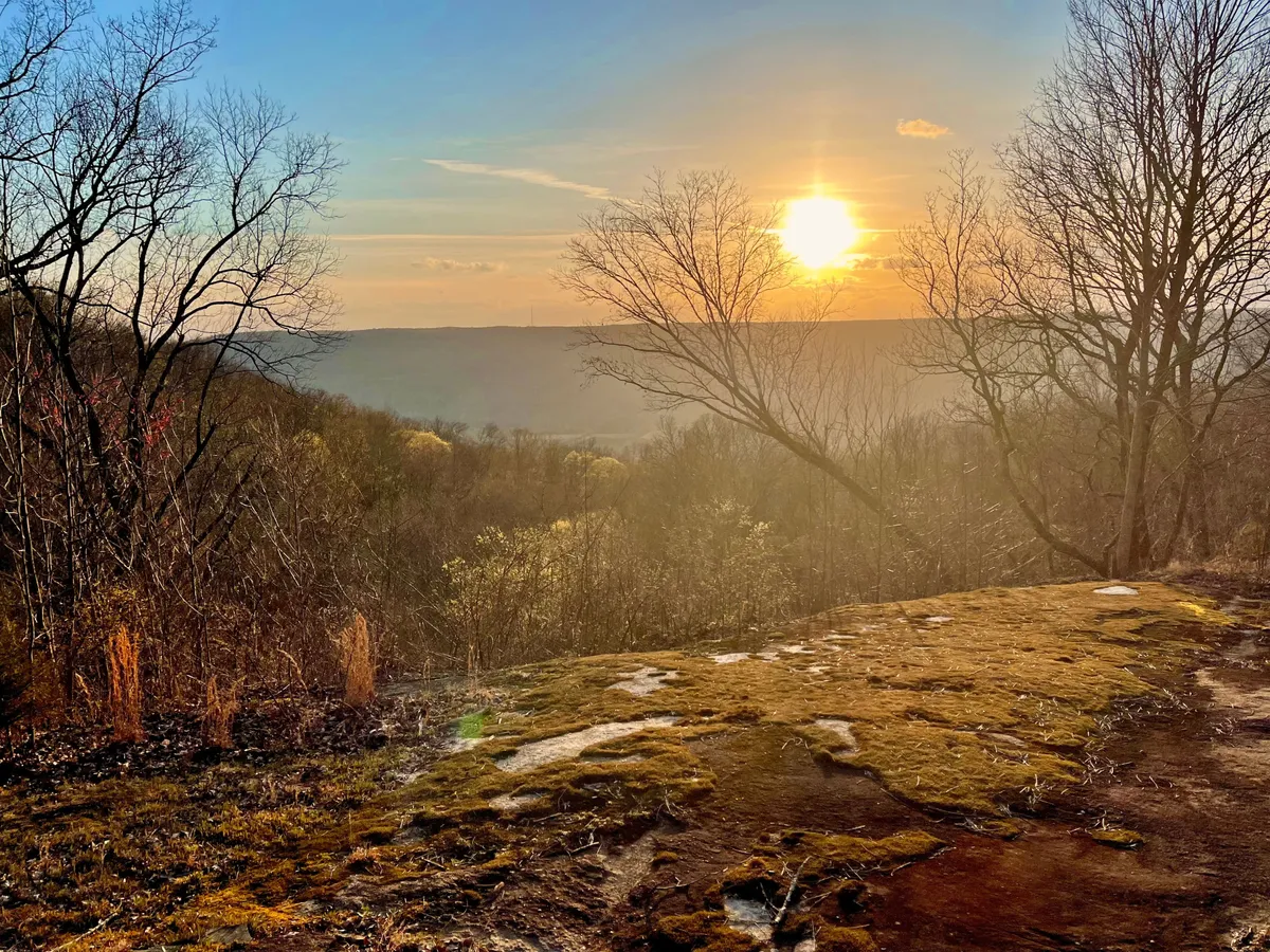 This image captures a breathtaking sunset over the treetops, with silhouettes of trees and a rocky foreground suggesting an elevated vantage point. The scene evokes serenity and a sense of awe, typical of the dramatic vistas found on renowned hiking trails.